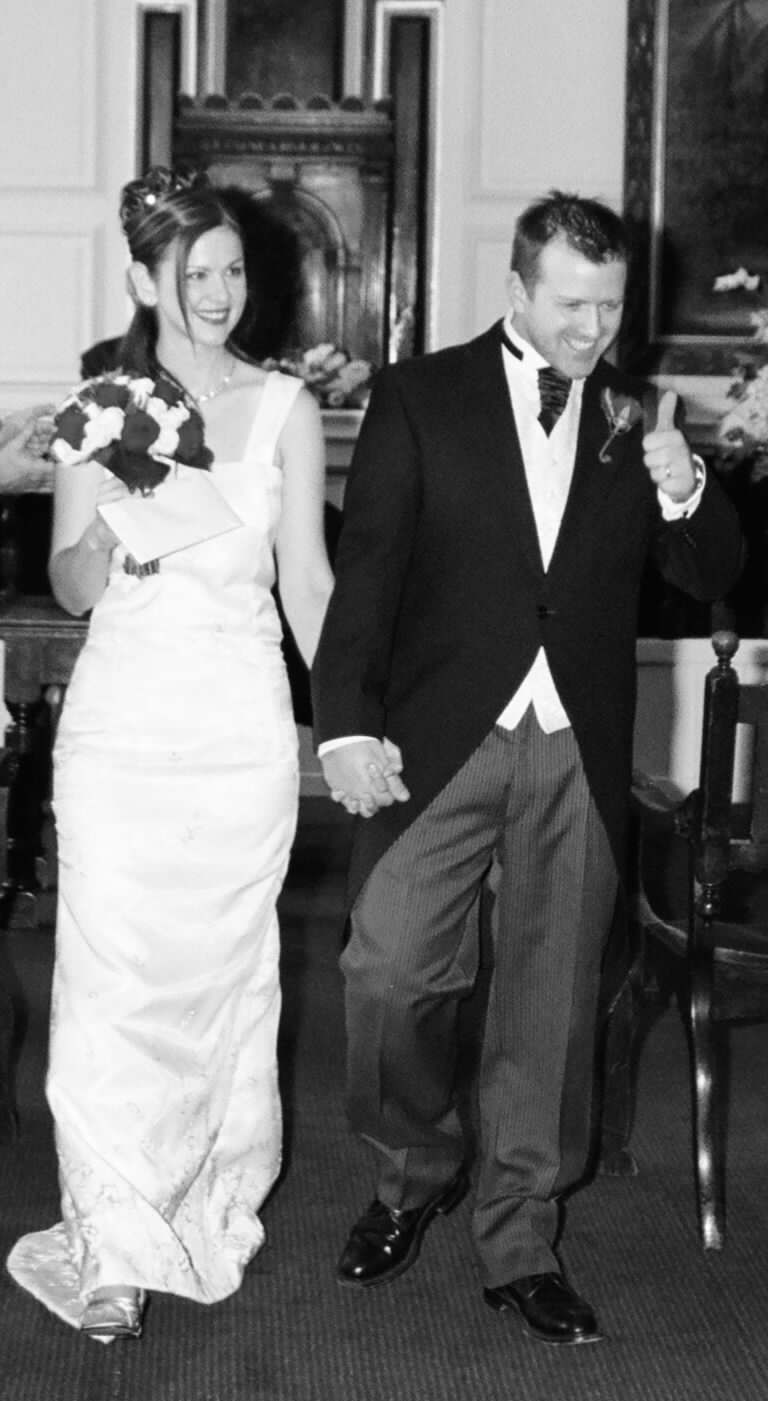 Heidi and her husband on their wedding day, walking hand in hand as he gives a thumbs up